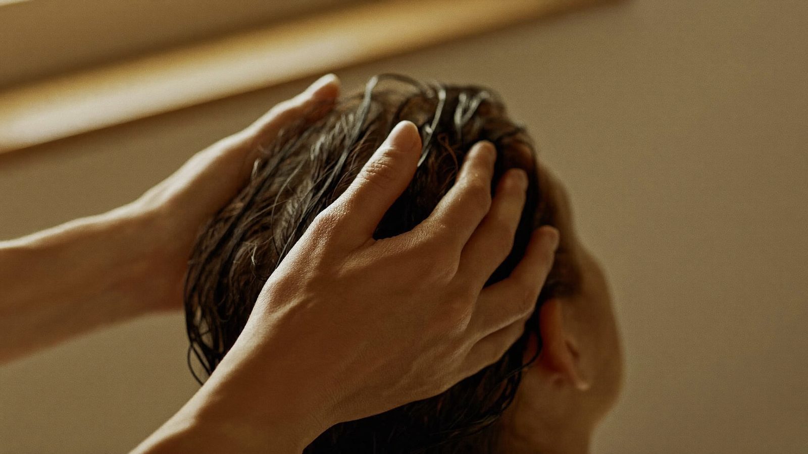 Nahaufnahme zweier Hände, die während einer Head-Spa-Behandlung mit den Fingerkuppen die Kopfhaut in feuchtem Haar massieren