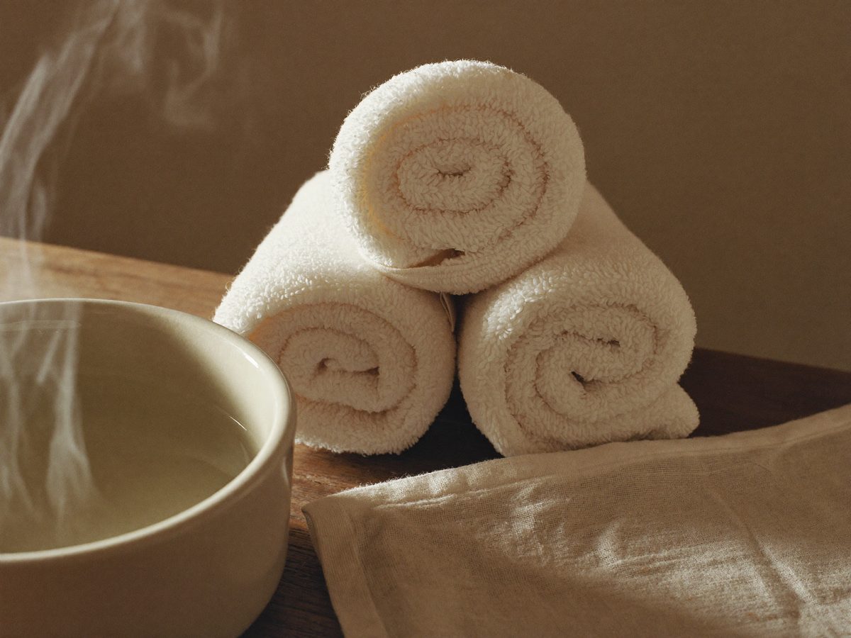 Detailaufnahme gerollter warmer Handtücher und einer weißen Keramikschale auf dunklem Holz in einem Spa